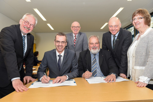 Jörg Bierwirth (l., in seiner Eigenschaft als Vorsteher des Zweckverbands Volkshochschule Lippe-Ost) und Dr. Bodo de Vries (stellvertretender Vorstandsvorsitzender des Ev. Johanneswerks) setzen die Unterschriften unter den Vertrag, flankiert von Bürgermeisterin Monika Rehmert (v.r., Extertal), Bürgermeister Klaus Geise (Blomberg), Bürgermeister Heinrich Josef Reker (Lügde) und Johanneswerk-Geschäftsführer Udo Ellermeier (Region Herford-Lippe). Foto: Johanneswerk/Christian Weische