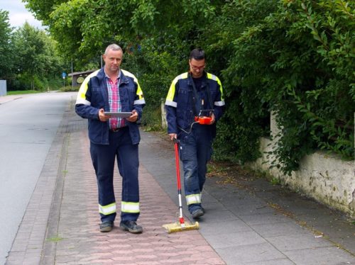Zwei Mitarbeiter überprüfen mit einem Gasspürgerät die Erdgasleitungen in einer Straße.