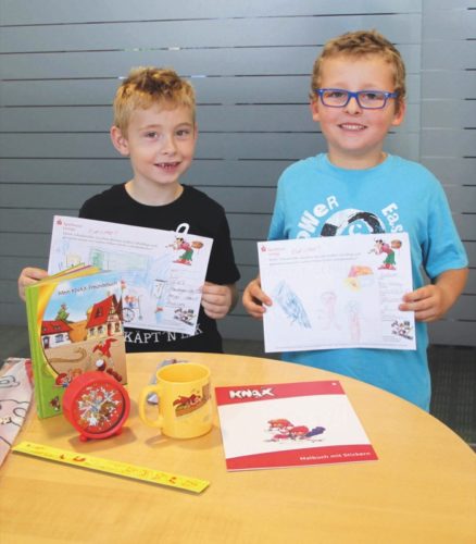 Zum Foto (von links): Die Gewinner Frederik Sieker und Ben-Henry Großert zeigen stolz ihre Bilder und freuen sich über ihr persönliches Knax-Schulpaket.