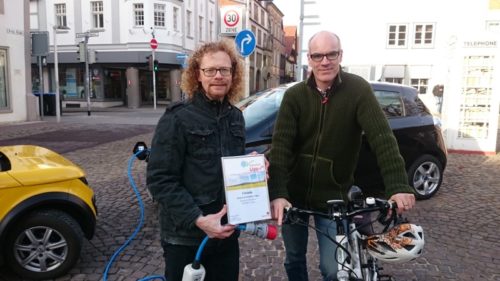 Foto: Ralf Kersting und Burkhard Pohl (Grüne Fraktion) präsentieren die Klimapakt-Urkunde und ihren Elektrofuhrpark